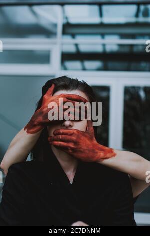red painted hands covering the eyes and mouth of a female. Concept of silence Stock Photo