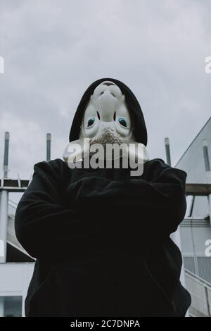 Vertical shot of a black hooded person wearing white sheep mask upside down Stock Photo