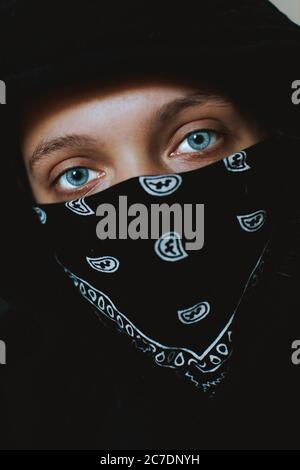 Vertical closeup shot of a blue eyes Caucasian person covering the mouth with black bandana Stock Photo