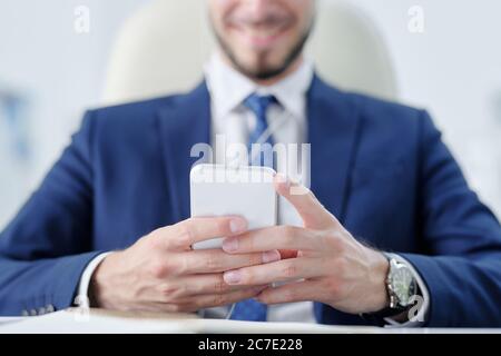 Close-up of businessman in suit using smartphone while texting message to colleague Stock Photo