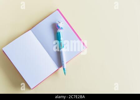 Pink notebook for notes, funny unicorn pen on yellow pastel background. Flat lay. Top view. Copy space Stock Photo