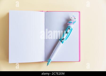 Pink notebook for notes, funny unicorn pen on yellow pastel background. Flat lay. Top view. Copy space Stock Photo