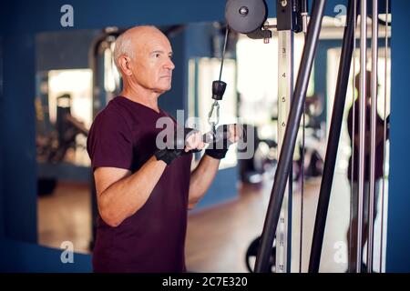 A portrait of bald senior man in the gym training arms muscles. People, health and lifestyle concept Stock Photo