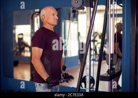 A portrait of bald senior man in the gym training arms muscles. People, health and lifestyle concept Stock Photo