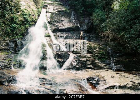 Wide shot of waterfall flowing down a rocky valley surrounded by trees Stock Photo