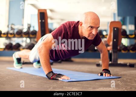 A portrait of bald senior man doing pushups exercise in the gym. People, healthcare and lifestyle concept Stock Photo