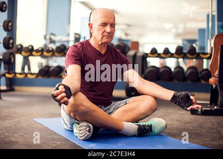 A portrait of bald senior man doing relaxation exercise in the gym. People, healthcare and lifestyle concept Stock Photo