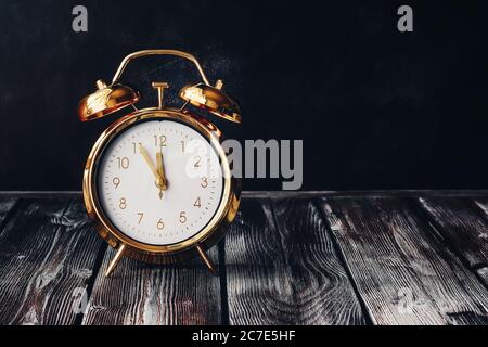 Gold alarm clock on a vintage wooden dark table. Rustic style. Selective focus, copy space. Time five minutes to twelve