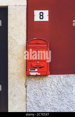 Vertical closeup shot of a red mailbox with the city crest engraved on it and a house plaque above Stock Photo