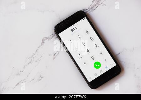 High angle shot of a turned-on black smartphone displaying 911 isolated on a white marble surface Stock Photo