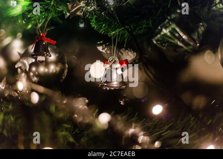 Horizontal selective closeup shot of silver bells hanging on the Christmas tree with bokeh lights Stock Photo