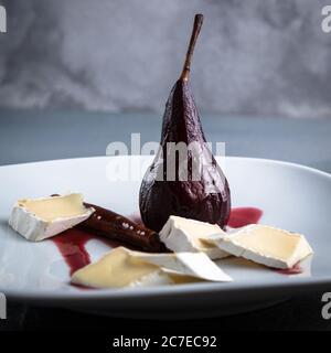 Red Wine Poached Pears in the white plate with cheese and cinnamon Stock Photo