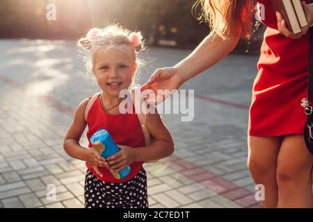 Mother brought daughter to school. Woman gives kid snacks and books checking backpack Stock Photo