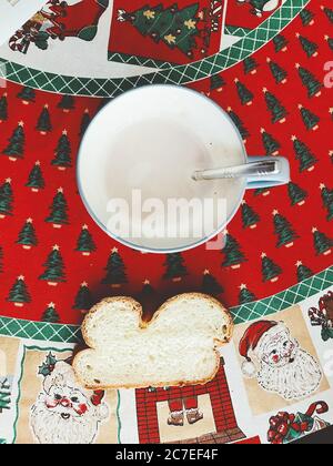 A cup of chocolate milk and a slice of bread on a Christmas-themed table clothing Stock Photo