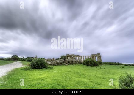 Wide shot of isolated abandoned building ruins in a green field under the dark cloudy sky Stock Photo
