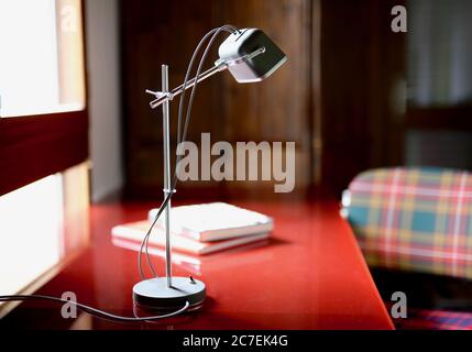 Selective focused shot of a gray and white articulated desk lamp on a red table Stock Photo