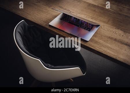 High angle shot of a grey silver laptop on a wooden desk with a white chair next to it Stock Photo
