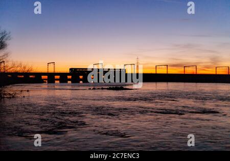 Scotrail class 156 sprinter train crossing the river Esk railway viaduct at Mossband on the  west coast mainline making a sunset silhouette. Stock Photo