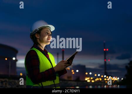 Asian woman petrochemical engineer working at night with digital tablet Inside oil and gas refinery plant industry factory at night for inspector safe Stock Photo