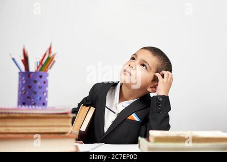 Thoughtful school boy scratching head and thinking on new ideas. Primary school pupil thinking, creating, brainstorming, trying to make right decision Stock Photo