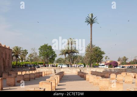 Guided tourist groups on the edge of the runis of the first Kutubiyya Mosque (1146) in central Marrakech, Morocco. There is a mobile phone mask in a t Stock Photo