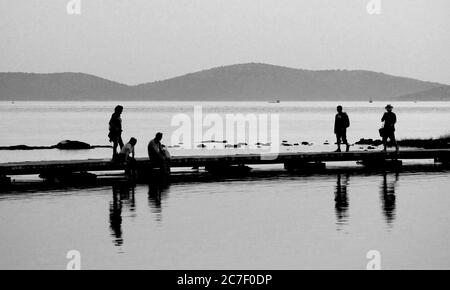 Beautiful shot of people on a pathway above the water in black and white Stock Photo