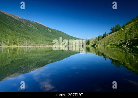 Wide shot of the Kanas lake surrounded by beautiful green mountains In China under the blue sky Stock Photo