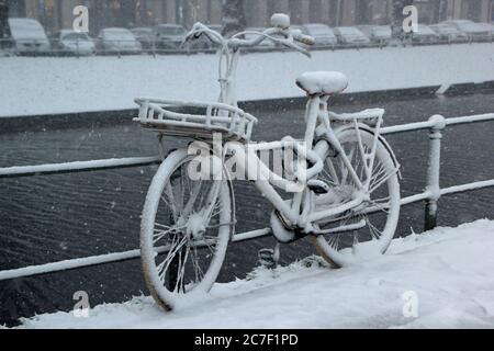 Bicycle leaned against a fence near the water covered in snow Stock Photo