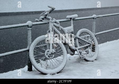 Bicycle leaned against a fence covered in snow Stock Photo