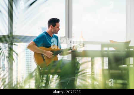 Portrait Of Man Playing Classic Guitar And Singing At Home Stock Photo