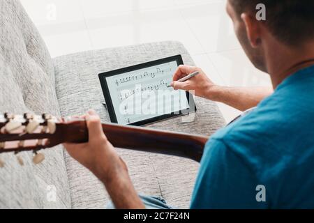 Man Composing Acoustic Guitar Sheet Music On Digital Tablet Stock Photo