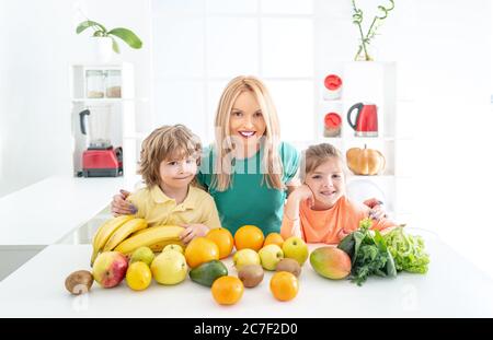 Happy laughing children and her beautiful young mother making fresh strawberry and other fruit juice in kitchen. Happy loving family. Stock Photo