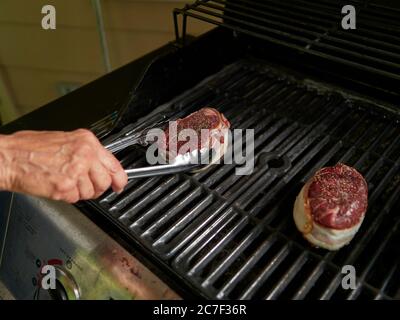 Woman cook or chef with tongs handling a thick filet cut steak on a gas barbecue grill, grilling the steak to put food on the table. Stock Photo