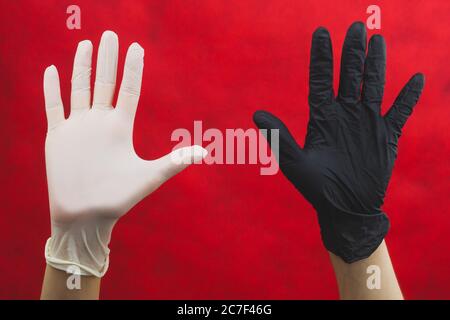 Hands raised up in protective gloves. one hand in black glove, other in white. gesturing hands in disposable gloves on a red background Stock Photo