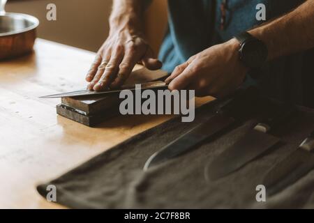 Person sharpening knives with a whetstone in the kitchen Stock Photo