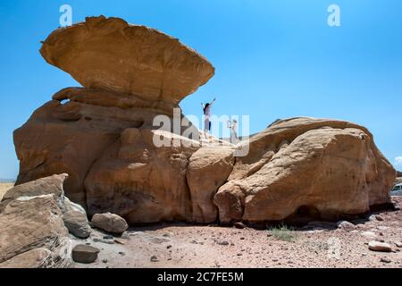 Tourists stand on Mushroom Rock in Wadi Rum in Jordan. Also known as the Valley of the Moon, Wadi Rum is a valley cut into sandstone and granite rock. Stock Photo