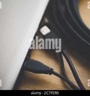 part of a silver laptop with usb wires and a skein of hdmi on a table. Stock Photo