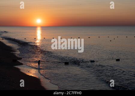 Awesome dawn over calm sea on beach landscape with nobody. Sunrise seascape with surf waves and buoy silhouettes in calm water Stock Photo