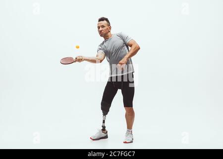 Athlete with disabilities or amputee isolated on white studio background. Professional male table tennis player with leg prosthesis training in studio. Disabled sport and healthy lifestyle concept. Stock Photo