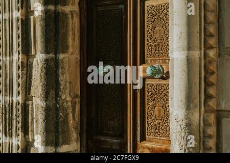 Detail of closed old wooden carved ornamental doors of the church with copper round handle covered with verdigris on sun light Stock Photo