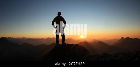 Man Silhouette reaching summit enjoying freedom and looking towards mountains sunset. Allgau Alps, Bavaria, Germany and Tyrol Austria. Stock Photo
