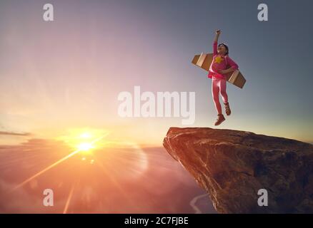 Little girl is playing astronaut. Child on the background of sunset sky. Kid in costume is dreaming of becoming a spaceman. Stock Photo