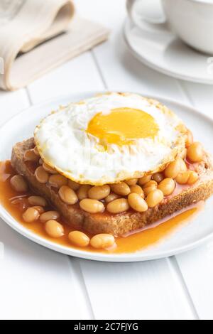 Toast with fried egg and baked beans on plate.