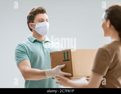 Delivery man in medical rubber gloves and mask. Online shopping. Quarantine. Woman accepting boxes from courier. Stock Photo