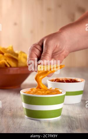 One person dips tortilla chips in nacho sauce. Stock Photo