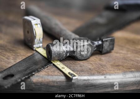 Close-up, shallow focus of an extended measuring tape showing the scales. Also are an old hammer and wood saw seen on an old, wooden workshop table. Stock Photo