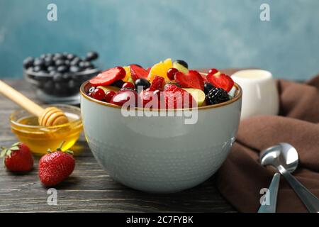 Composition with bowl of fresh fruit salad on wooden background, close up