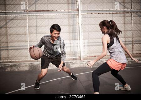young asian adult man and woman having fun playing basketball on a outdoor court Stock Photo