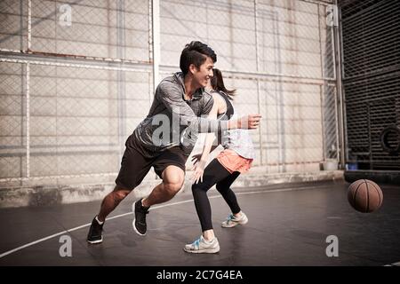 young asian adult man and woman having fun playing basketball on a outdoor court
