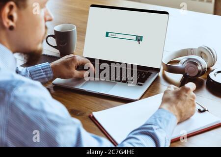 Search bar, copyspace on laptop screen. Man looking for job home during COVID-19 quarantine, remote office concept. Unemployed guy sitting in front of monitor, writing a resume, doing notes. Stock Photo